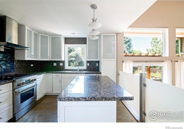 kitchen with wall chimney exhaust hood, dark hardwood / wood-style flooring, high end stainless steel range oven, and a wealth of natural light