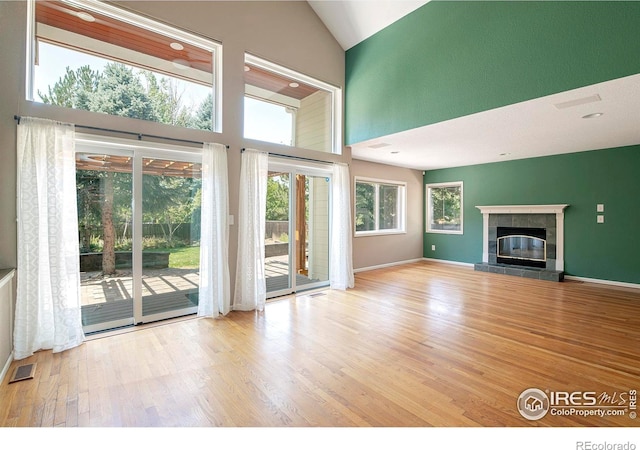 unfurnished living room featuring a tile fireplace, high vaulted ceiling, and light hardwood / wood-style flooring