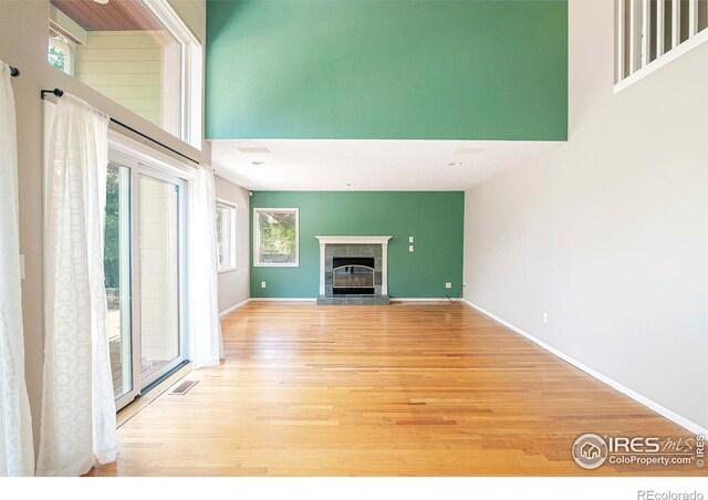 unfurnished living room featuring light wood-type flooring, a high ceiling, and a tile fireplace