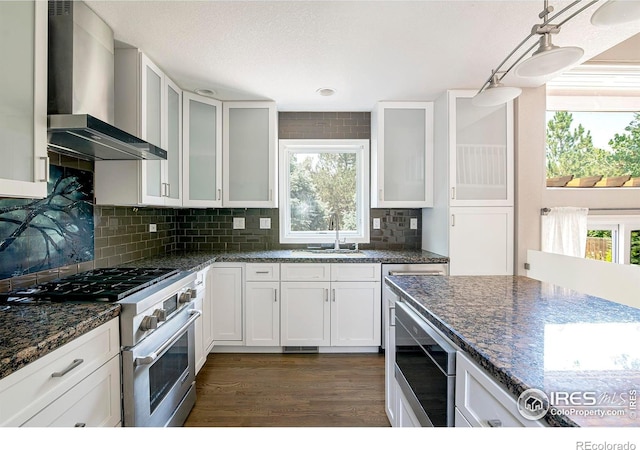 kitchen with white cabinets, wall chimney range hood, range with gas cooktop, decorative light fixtures, and dark hardwood / wood-style flooring