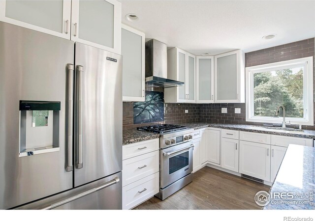 kitchen featuring hardwood / wood-style floors, premium appliances, sink, backsplash, and wall chimney range hood