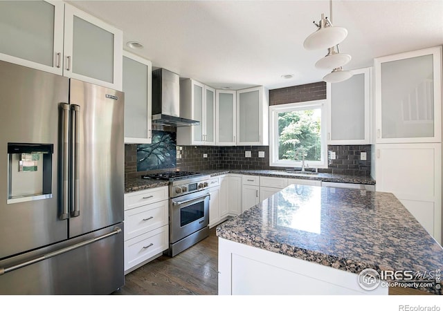 kitchen with decorative light fixtures, dark stone countertops, dark hardwood / wood-style flooring, premium appliances, and wall chimney exhaust hood