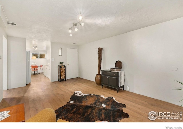 living room with track lighting, a textured ceiling, and light hardwood / wood-style floors