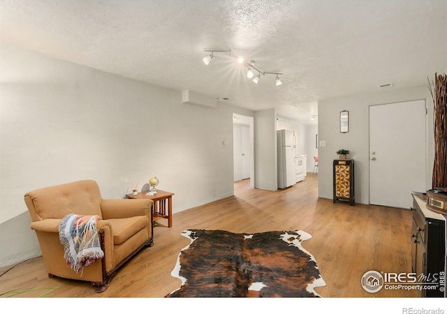 living room featuring rail lighting, a textured ceiling, and light hardwood / wood-style floors