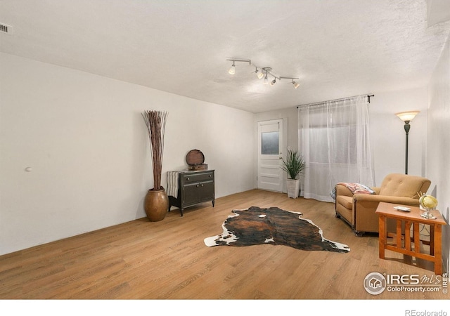 living room with track lighting, a textured ceiling, and light hardwood / wood-style floors