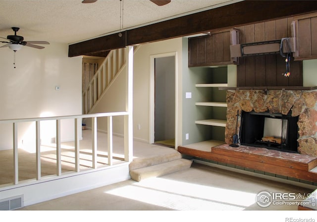 unfurnished living room with ceiling fan, carpet, a stone fireplace, and a textured ceiling