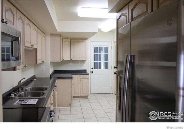 kitchen featuring dark countertops, light tile patterned floors, appliances with stainless steel finishes, and a sink