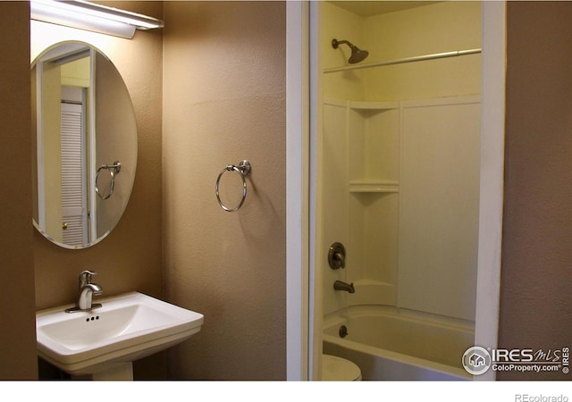 bathroom featuring shower / washtub combination, toilet, a textured wall, and a sink