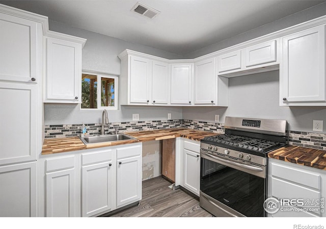 kitchen featuring stainless steel gas stove, decorative backsplash, white cabinets, and a sink