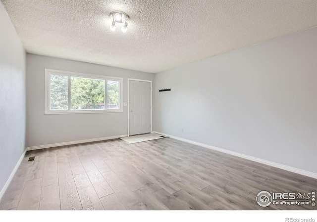 unfurnished room featuring light wood-type flooring, visible vents, baseboards, and a textured ceiling