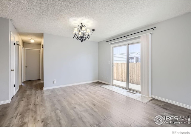 spare room with light hardwood / wood-style floors, a textured ceiling, and an inviting chandelier