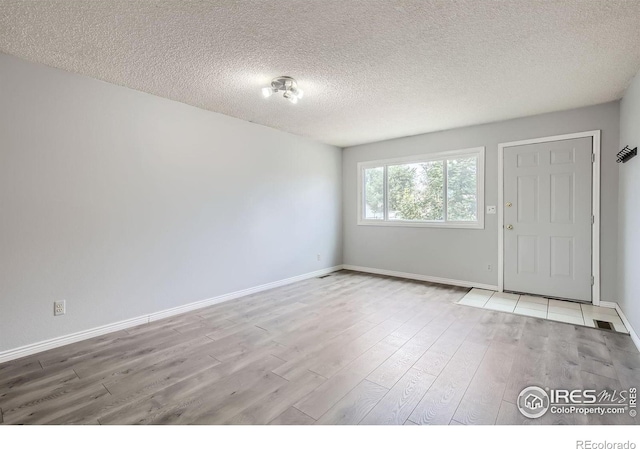 unfurnished room featuring visible vents, light wood-style flooring, baseboards, and a textured ceiling