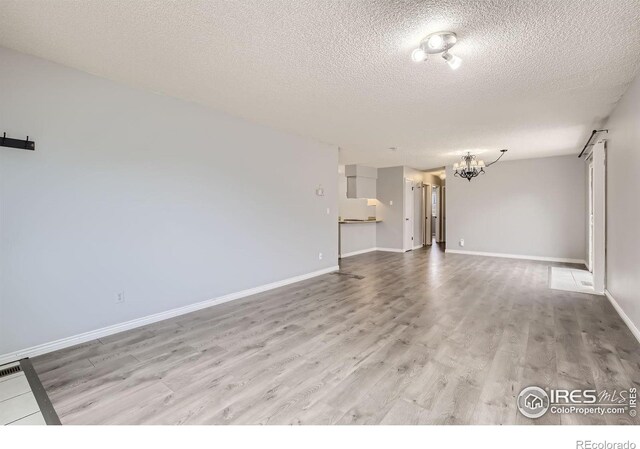 unfurnished living room with light wood finished floors, a textured ceiling, baseboards, and a notable chandelier