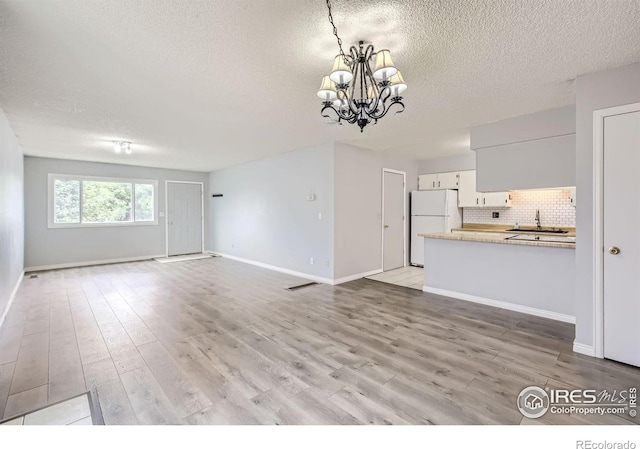 unfurnished living room with a textured ceiling, light wood-style flooring, a notable chandelier, a sink, and baseboards