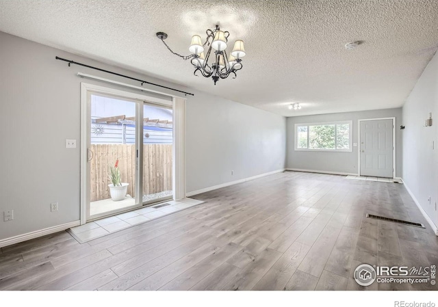 empty room featuring light wood-type flooring, a notable chandelier, a textured ceiling, and baseboards