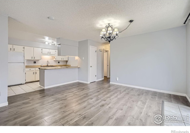 kitchen featuring white cabinetry, backsplash, kitchen peninsula, white fridge, and a chandelier