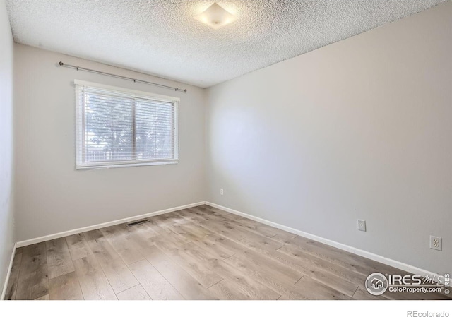 unfurnished room featuring a textured ceiling, light wood-style flooring, visible vents, and baseboards