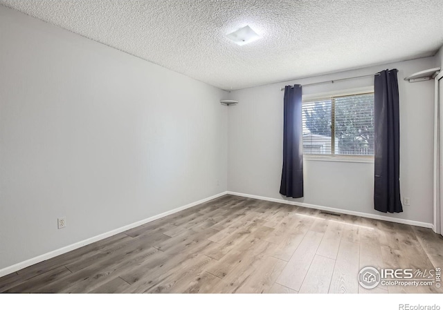 empty room with a textured ceiling, visible vents, light wood-style flooring, and baseboards