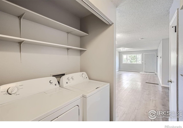 clothes washing area featuring washer and dryer, light hardwood / wood-style floors, and a textured ceiling