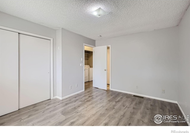 unfurnished bedroom with a textured ceiling, separate washer and dryer, light hardwood / wood-style flooring, and a closet