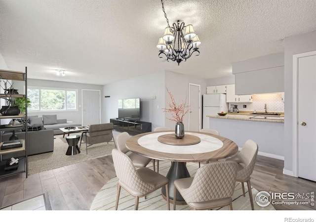 dining space featuring a notable chandelier, light wood-style flooring, and a textured ceiling