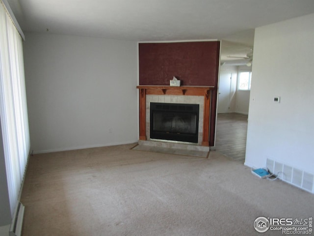 unfurnished living room featuring ceiling fan, a tiled fireplace, and carpet floors