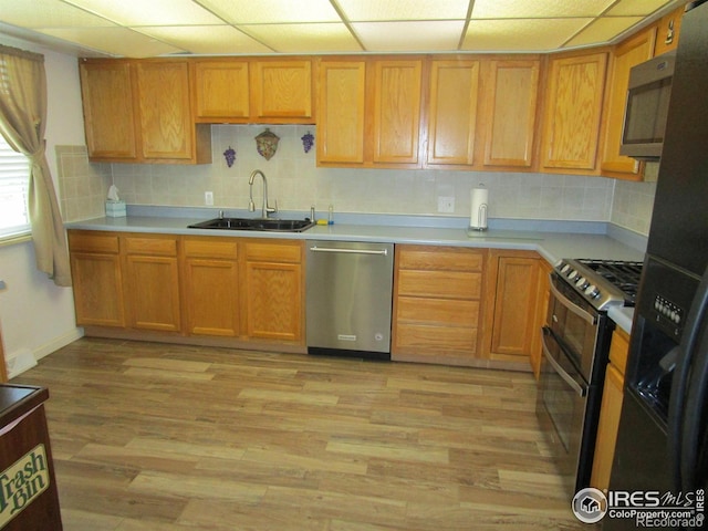 kitchen with a paneled ceiling, appliances with stainless steel finishes, light wood-type flooring, tasteful backsplash, and sink