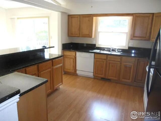 kitchen featuring sink, light wood-type flooring, white dishwasher, and black refrigerator