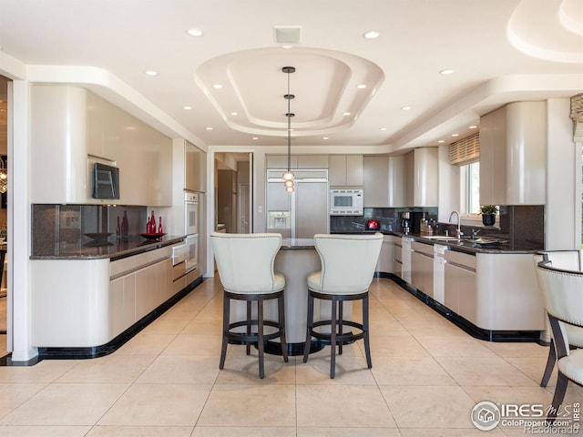 kitchen featuring built in appliances, a kitchen breakfast bar, a raised ceiling, tasteful backsplash, and a sink