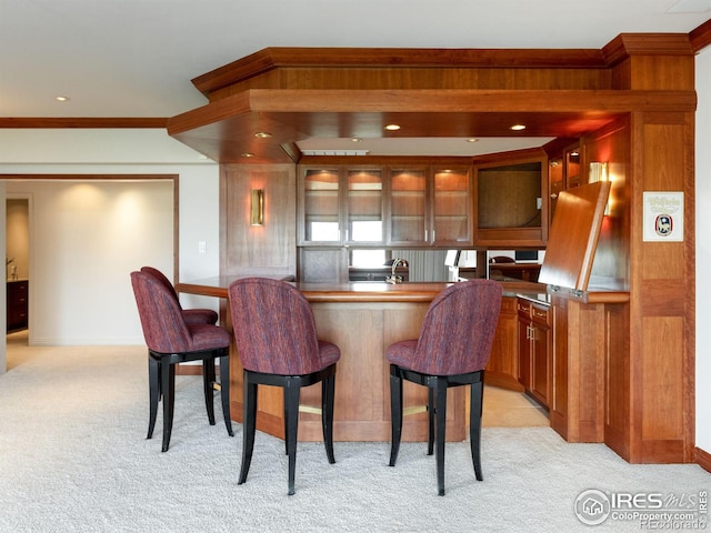 kitchen featuring light colored carpet, baseboards, a kitchen breakfast bar, and glass insert cabinets