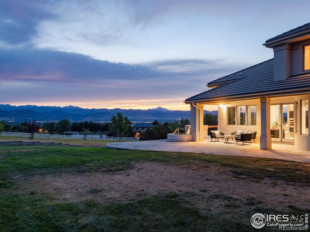 exterior space featuring fence, a mountain view, a patio area, a lawn, and a tiled roof