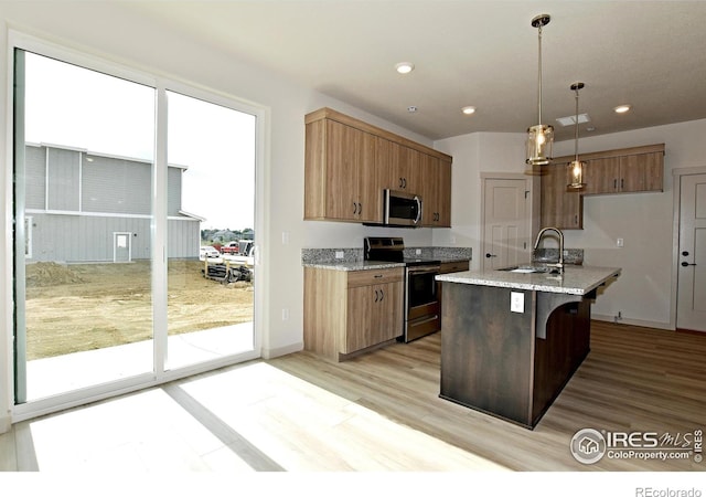 kitchen featuring sink, light stone counters, an island with sink, pendant lighting, and stainless steel appliances