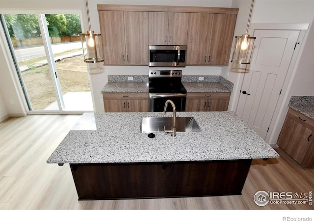 kitchen with stainless steel appliances, a kitchen island with sink, sink, and light stone countertops