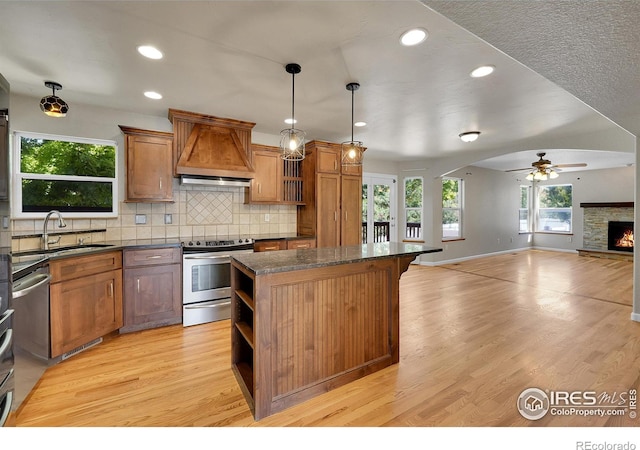 kitchen featuring stainless steel appliances, decorative light fixtures, light hardwood / wood-style flooring, a center island, and premium range hood