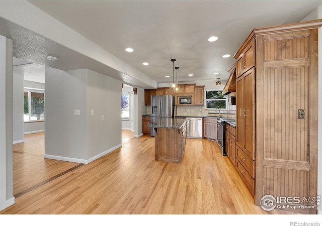 kitchen with light hardwood / wood-style floors, a center island, stone countertops, appliances with stainless steel finishes, and decorative light fixtures