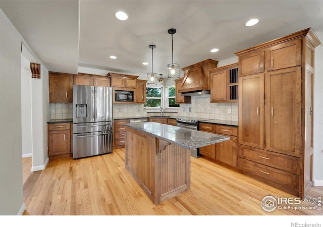 kitchen featuring stainless steel appliances, light hardwood / wood-style floors, hanging light fixtures, sink, and premium range hood