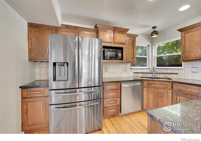 kitchen featuring tasteful backsplash, stainless steel appliances, sink, light hardwood / wood-style floors, and dark stone countertops