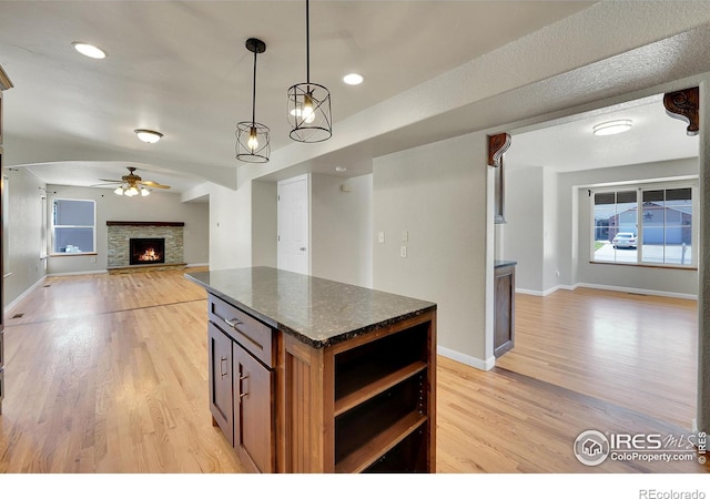 kitchen with dark stone counters, hanging light fixtures, a fireplace, light hardwood / wood-style flooring, and a center island