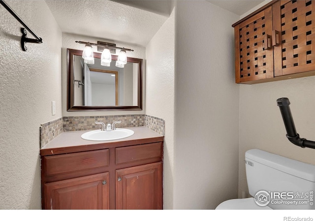 bathroom with tasteful backsplash, vanity, a textured ceiling, and toilet