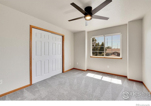 unfurnished bedroom featuring a closet, a textured ceiling, carpet flooring, and ceiling fan