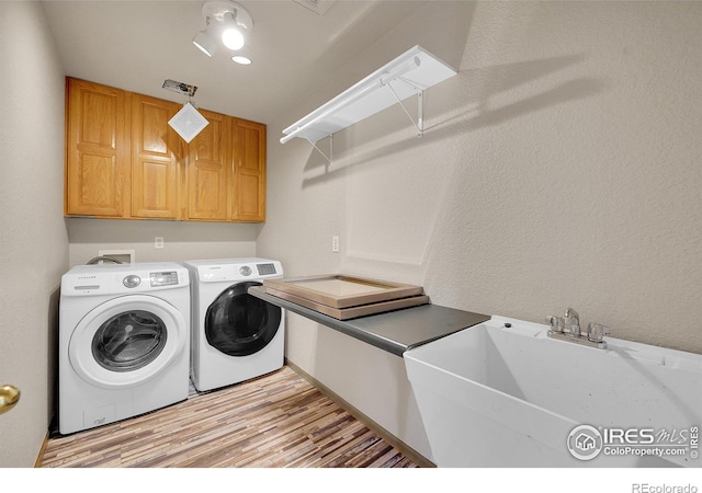 laundry room with cabinets, sink, washer and dryer, and light hardwood / wood-style flooring