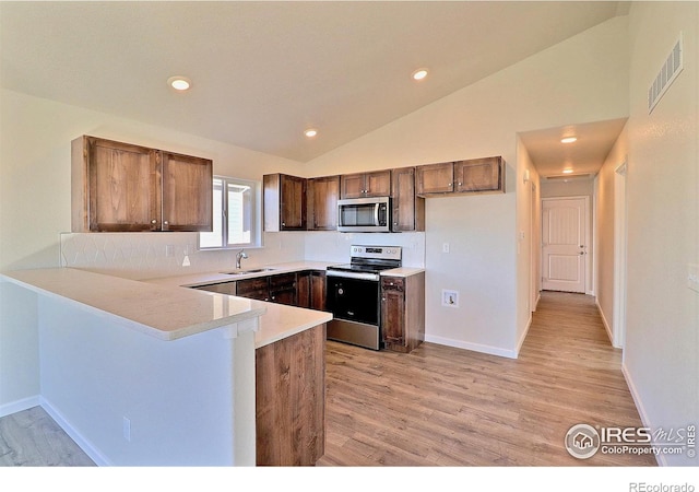 kitchen featuring lofted ceiling, sink, light hardwood / wood-style floors, kitchen peninsula, and stainless steel appliances