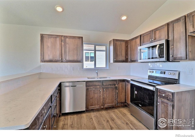 kitchen featuring kitchen peninsula, sink, appliances with stainless steel finishes, and vaulted ceiling