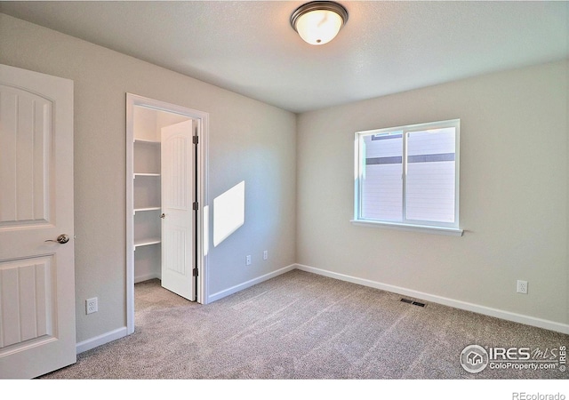 unfurnished bedroom with a walk in closet, light carpet, and a closet