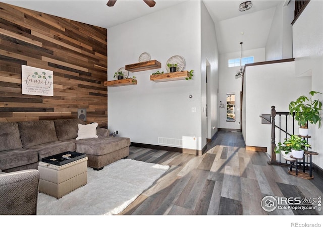 living room with ceiling fan, dark hardwood / wood-style floors, wood walls, and high vaulted ceiling