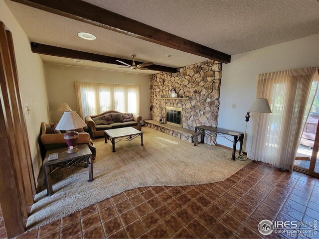 tiled living room with ceiling fan, a textured ceiling, a fireplace, and beamed ceiling