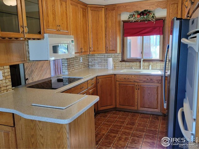 kitchen featuring decorative backsplash, black electric stovetop, sink, dark tile patterned floors, and refrigerator