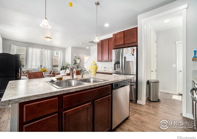 kitchen with pendant lighting, a center island with sink, light hardwood / wood-style floors, stainless steel appliances, and sink