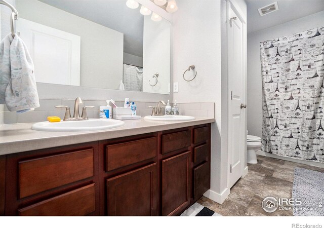 bathroom featuring tasteful backsplash, double vanity, tile patterned flooring, and toilet