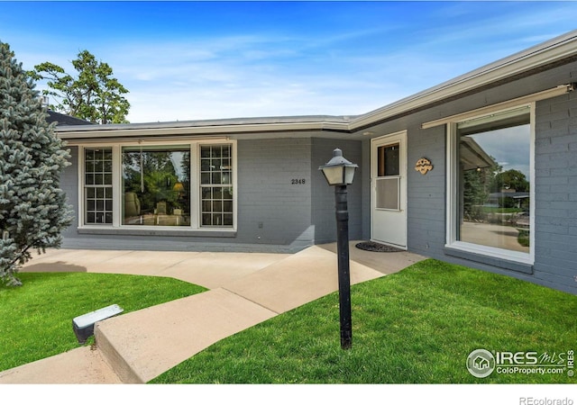 entrance to property featuring brick siding, a patio, and a yard